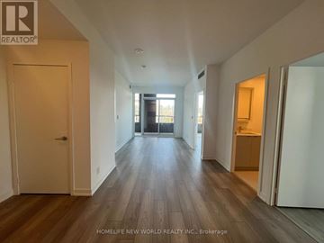 Toronto (South Parkdale) condo for rent - A spacious room with wooden floors and white walls, with a door on the left and a kitchen area on the right.