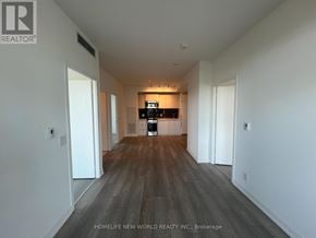 Toronto (South Parkdale) condo for rent - A spacious room with wooden flooring and white walls.
