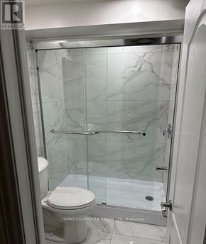 Oshawa (Lakeview) apartment for rent - A white toilet is in a marble bathroom with a glass shower door.
