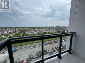 Clarington (Bowmanville) condo for rent - A balcony overlooks a parking lot and buildings.