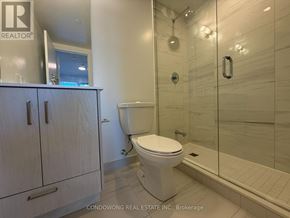 Toronto (Moss Park) condo for rent - A white toilet in a modern bathroom with a glass shower stall.