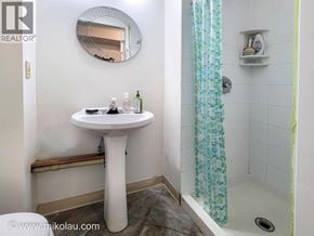 Vancouver apartment for rent - A white pedestal sink in a small bathroom with a round mirror and a shower with a blue curtain.