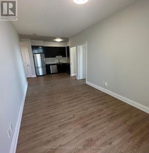 Markham (Grandview) condo for rent - A room with wooden flooring and white walls, with a kitchen area visible in the background.