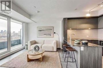 Toronto (Regent Park) condo for rent - A modern living room with a large window and a kitchen area in the background.