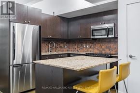 Toronto (South Riverdale) condo for rent - A kitchen with a refrigerator, microwave, and a table with yellow chairs.