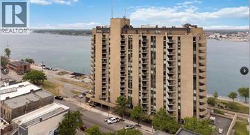 Sarnia condo for rent - A tall building with a balcony on the 10th floor is in the foreground of a city street.