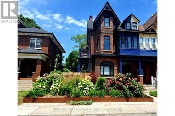 Toronto (Dufferin Grove) fourplex for rent - A large house with a blue front door and a flower bed in front.