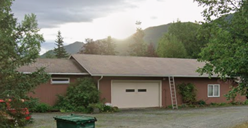 Eagle River apartment for rent - A house with a brown roof and a white garage door is surrounded by greenery.