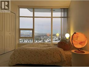 Burnaby apartment for rent - A bedroom with a large window overlooking a cityscape.