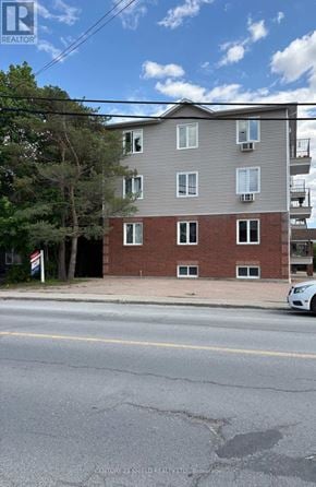Russell condo for rent - A multi-story building with a brick base and a grey upper section is situated on a street corner.