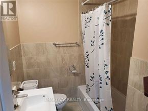 Mississauga (Meadowvale Village) apartment for rent - A bathroom with a toilet, a shower curtain with a leaf pattern, and a tiled wall.
