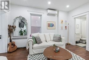 Toronto (Roncesvalles) multi-family for rent - A living room with a white couch, a guitar, a mirror, and a coffee table.