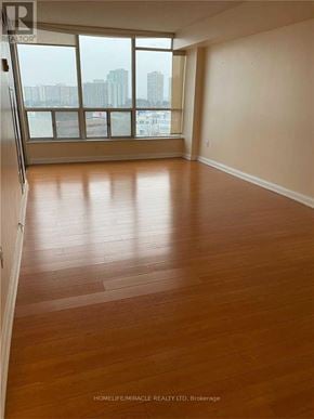 Brampton (Queen Street Corridor) condo for rent - A room with wooden flooring and a large window overlooking a cityscape.