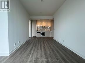 Toronto (Moss Park) condo for rent - A spacious room with wood flooring and a kitchen area in the background.