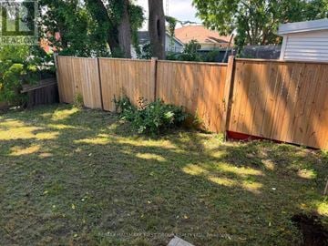 Oshawa (O'neill) triplex for rent - A backyard with a wooden fence and green grass.