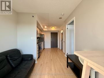 Toronto (Little Portugal) condo for rent - A black couch sits in a living room with a wooden floor and white walls.