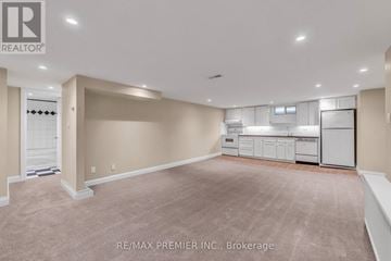 Toronto (Forest Hill South) duplex for rent - A spacious room with beige carpeting and white walls, featuring a kitchenette with white appliances.