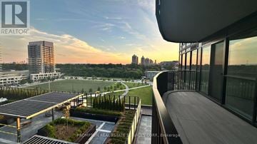 Toronto (Bayview Village) condo for rent - A modern building with a balcony overlooking a cityscape at sunset.