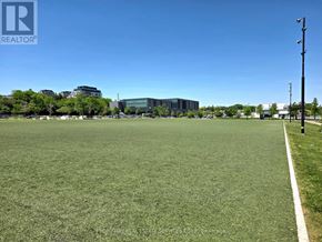 Toronto (Bayview Village) condo for rent - A grassy field with a white line on it and buildings in the background.