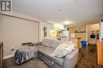 Guelph (Kortright West) apartment for rent - A living room with a grey couch and a kitchen area in the background.