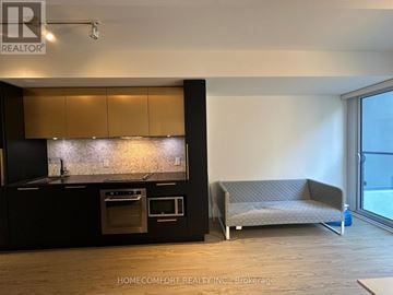 Toronto (Church-Yonge Corridor) condo for rent - A modern kitchen with a black countertop and a grey sofa in the living room.