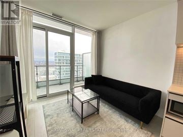 Vaughan (Vaughan Corporate Centre) condo for rent - A black sofa sits in a living room with a glass table and a balcony with a view of the city.