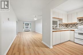 Toronto (Long Branch) condo for rent - A white room with wooden floors and a kitchen area with white cabinets and a stone backsplash.