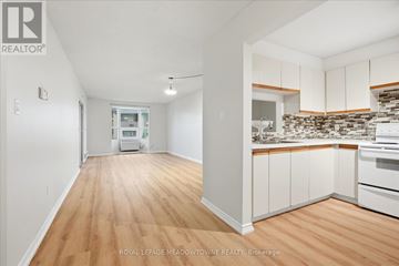 Toronto (Long Branch) condo for rent - A white room with wooden floors and a kitchen area with white cabinets and a stone backsplash.