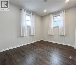 Lakeshore apartment for rent - A room with wooden floors and two windows with white curtains.