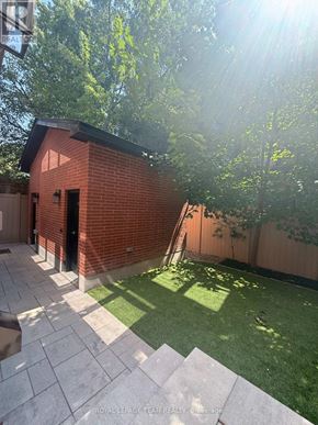 Ottawa apartment for rent - A small red brick building with a black door is surrounded by a green lawn and trees.