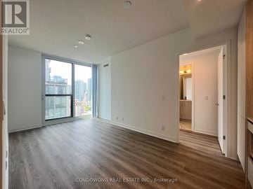 Toronto (Moss Park) condo for rent - A spacious room with wood flooring and a large window overlooking a cityscape.