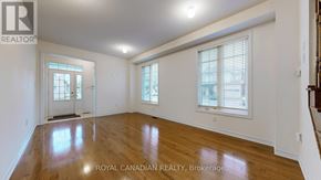 Whitchurch-Stouffville (Stouffville) apartment for rent - A spacious room with wooden floors and white walls, with a door on the left and a window with blinds on the right.