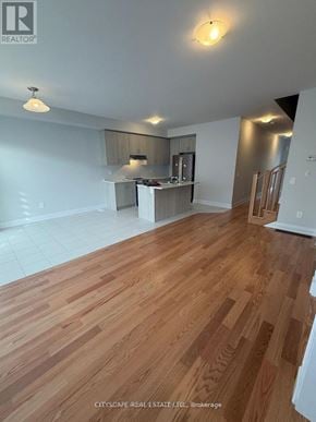 Kawartha Lakes (Lindsay) townhouse for rent - A spacious room with wooden flooring and a kitchen area in the background.