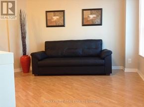 Toronto (Woburn) condo for rent - A black couch sits in a room with a wooden floor and two pictures on the wall.