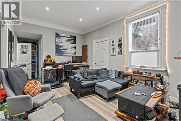 Hamilton apartment for rent - A living room with a grey couch, a grey armchair, a grey ottoman, a wooden coffee table, a TV on a stand, a bookshelf, a window with blinds, a painting on the wall, and a