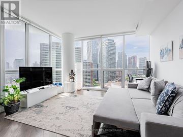 Toronto (Church-Yonge Corridor) condo for rent - A living room with a grey couch and a large window overlooking a cityscape.