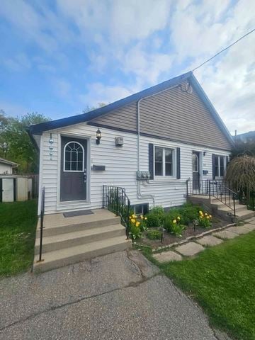 London apartment for rent - A house with a grey siding and a black door is surrounded by a small garden with yellow flowers.