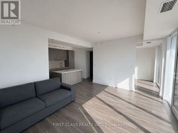 Toronto (Bay Street Corridor) condo for rent - A grey couch sits in a spacious living room with wood flooring and white walls.