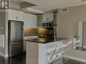 Ottawa condo for rent - A kitchen with a refrigerator, microwave, and a counter with chairs.
