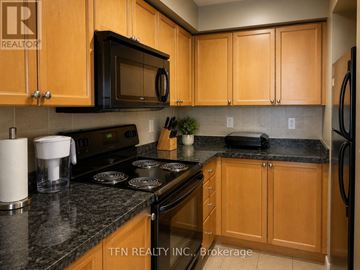 Mississauga (City Centre) condo for rent - A kitchen with wooden cabinets and a black countertop.