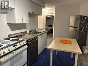 Vancouver apartment for rent - A kitchen with a stove top oven, a refrigerator with magnets, and a table with an orange towel on it.