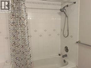 Vancouver apartment for rent - A white tiled bathroom with a shower curtain and a shower head.