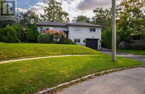 Barrie (Wellington) apartment for rent - A house with a grey roof and a black garage door is surrounded by green grass and trees.