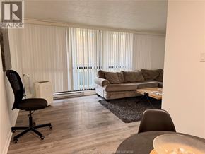 Windsor condo for rent - A living room with a brown couch, a black chair, and a white air conditioner unit.