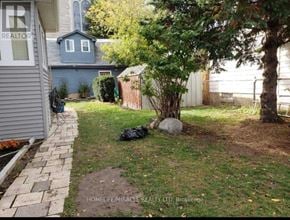 Oshawa (Central) apartment for rent - A backyard with a small tree, a rock, and a black bag.