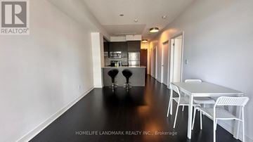 Mississauga (City Centre) condo for rent - A white dining table with four chairs is in a room with white walls and a kitchen in the background.