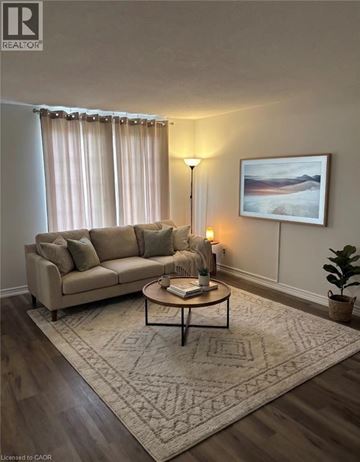 Hamilton condo for rent - A living room with a beige couch, a coffee table, a lamp, a rug, and a painting on the wall.