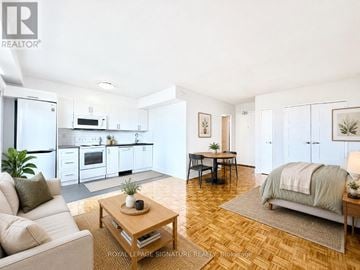 Toronto (Annex) condo for rent - A well-lit, spacious living room with a couch, coffee table, and a bed in the background.