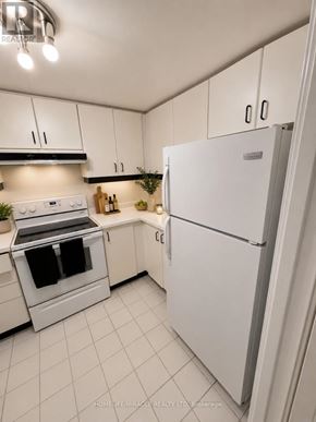 Toronto (Bay Street Corridor) condo for rent - A white refrigerator stands in a kitchen with white cabinets and a white stove.