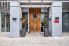 Toronto (Waterfront Communities) condo for rent - A room with wooden flooring and a kitchen area in the background.
